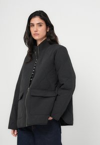 Μαύρο καπιτονέ μπουφάν με ψηλό γιακά, κλείσιμο με φερμουάρ και μπροστινές τσέπες. Διαθέτει υφή με ανάγλυφο σχέδιο και άνετη εφαρμογή.