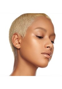 Zbliżenie modelki z krótkimi, platynowymi blond włosami, noszącej małe złote kolczyki wkręty, prezentującej gładką skórę z delikatnym połyskiem.