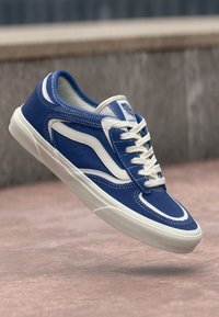 Blue sneaker featuring a leather upper with white accents, rounded toe, and raised rubber sole. Includes white laces and branding on the tongue.
