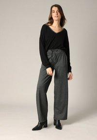 Haut noir à manches longues avec un décolleté en V, associé à un pantalon large à carreaux gris et des bottines, mettant en avant une coupe décontractée et une taille élastique réglable.