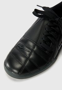 Schwarze Leder-Sneaker mit einem gesteppten Design, ausgestattet mit einer schwarzen Schnürung und einem auffälligen Logo an der Seite.