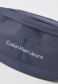 Sötétkék anyagú sapka lekerekített formával, a "Calvin Klein Jeans" logóval fehér színben. Simaságával és finom varrási részleteivel tűnik ki.