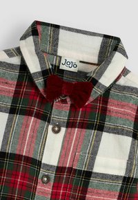 Camicia a quadri rossa e verde con base bianca, con un papillon in velluto rosso e un'etichetta che recita "JoJo." Tessuto di cotone testurizzato.