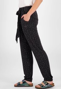 Černé kalhoty s uvázaným pasem, bočními kapsami a multibarevným skvrnitým vzorem. Spárovány s multibarevnými sandály na texturované podrážce.