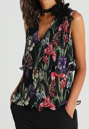 Sleeveless black blouse with red, purple, and white floral print, ruffled details at hem and chest, worn with black pants and floral choker.