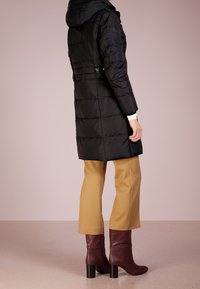 Svart puffjacka med huva, quiltat mönster och sidoknappar. Matchad med beige byxor och burgundy klackstövlar.