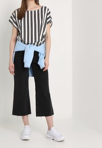 Sort og hvid stribet bluse, lyseblå sweatshirt bundet om taljen, sorte cropped bukser og hvide sportsko.