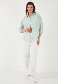 Green and white striped shirt, oversized fit, button closure, two chest pockets, paired with white wide-leg trousers and white sneakers.