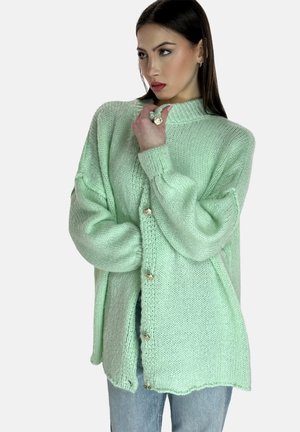 Pudergraue, oversized gestrickte Strickjacke mit langen Ärmeln, gerippten Bündchen und silbernen Knopfverschlüssen. Weicher Griff und unregelmäßiger Saum.