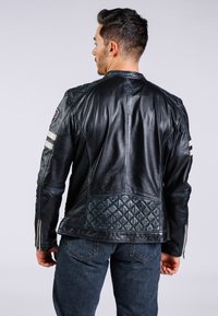 Chaqueta de cuero negra con panel trasero acolchado, acentos a rayas en los hombros y un diseño ajustado. Los puños con cremallera añaden detalle.