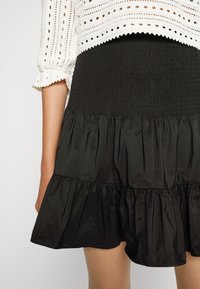 Vrouw in een zwarte gelaagde rok en een witte gehaakte top met driekwartmouwen, zichtbaar van het midden van de bovenbenen tot de taille.