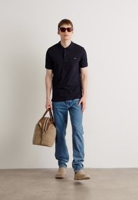 Tengerész polos shirt, világoskék farmer, bézs cipő és barna részletekkel díszített bézs táska. Sötét napszemüveg teszi teljessé a megjelenést. Egyszerű, hétköznapi összeállítás.