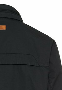 Schwarzjacke mit hohem Kragen, strukturiertem Stoff und einem braunen Etikett auf der Rückseite mit dezenten horizontalen Nahtdetails.