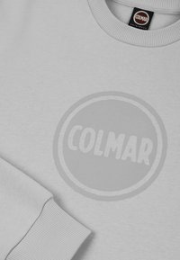 Gai pelēks sporta krekls no mīkstas auduma, ar smalku apaļu logotipu centrā, kurā ir vārds "COLMAR", un ribota apkakle un piedurknes.