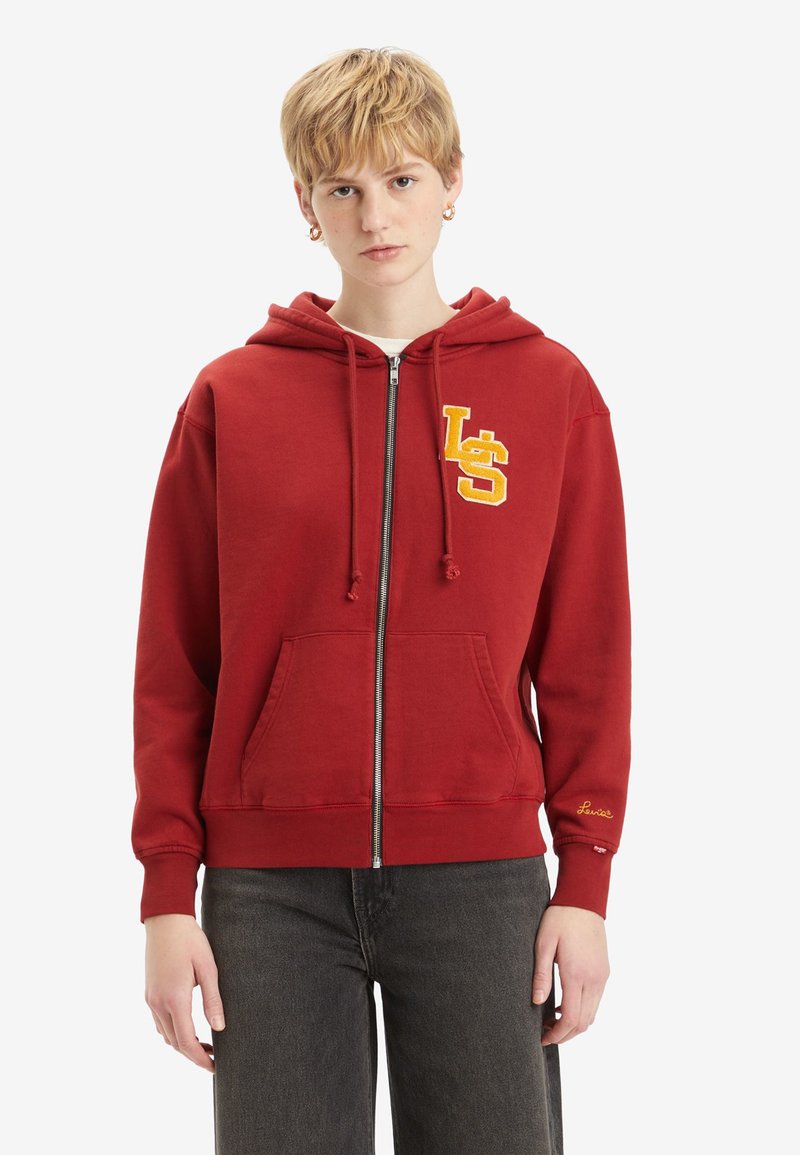 Hoodie rouge zippé avec une poche frontale. Présente une broderie "LS" jaune sur la poitrine gauche et "Lucile" brodé sur le poignet. Tissu doux.