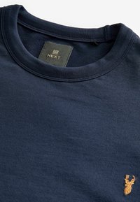Navyblauwe katoenen t-shirt met een ronde halslijn, voorzien van een klein, gouden hertembleem op de borst en een label met de tekst "NEXT" binnenin.