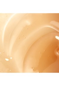 Gros plan sur un gel beige brillant et translucide avec de petites bulles d'air, montrant une texture lisse et fluide ainsi que des reflets de la lumière.
