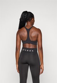 Top desportivo preto com um design de costas nadador, combinado com leggings pretas de cintura alta que apresentam um logo branco "HYROX" na cintura.