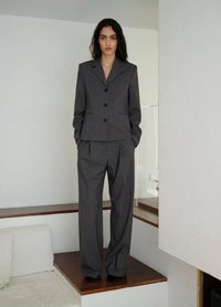 Op maat gemaakt donkergrijs kostuum met een getailleerde blazer met notch-kraag en een knoopsluiting, in combinatie met wijde broekspijpen. Gladde stoftextuur.
