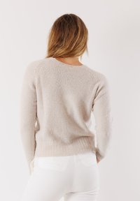 Maglione beige chiaro in tessuto morbido con texture, presenta maniche lunghe e un collo rotondo, accentuato da un sottile orlo a costine.
