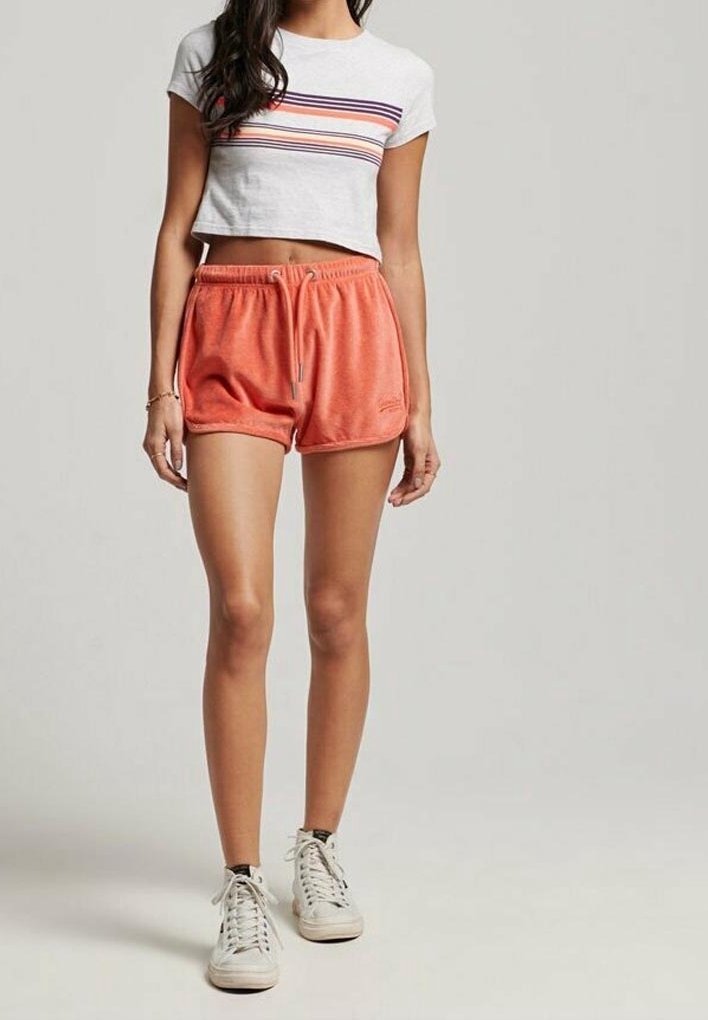 Maglietta grigia corta con strisce orizzontali multicolori, abbinata a pantaloni sportivi corallo con vita elastica e cordino. Sneakers bianche.