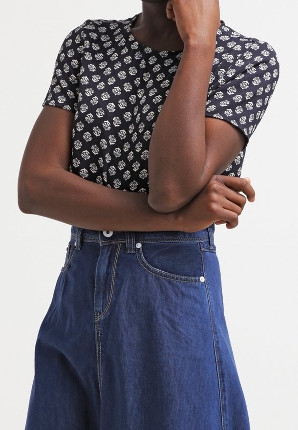 Haut à manches courtes bleu marine avec imprimé floral blanc, associé à un jean bleu taille haute avec poches avant et coutures dorées.