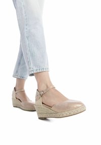 Zapatos de cuña metálicos en color beige con suela trenzada similar al yute, que presentan una correa alrededor del tobillo y un diseño de punta abierta.