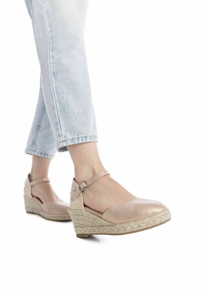 Zapatos de cuña metálicos en color beige con suela trenzada similar al yute, que presentan una correa alrededor del tobillo y un diseño de punta abierta.