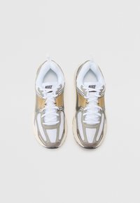 Baskets Nike avec une tige en mesh blanc, accents dorés et détails gris. Bout arrondi et système de laçage avec une languette au niveau du talon.