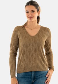 Maglione a maniche lunghe con scollo a V in un tessuto metallico dorato texturizzato con un motivo a onde. Abbinato a jeans blu, collana sottile visibile.