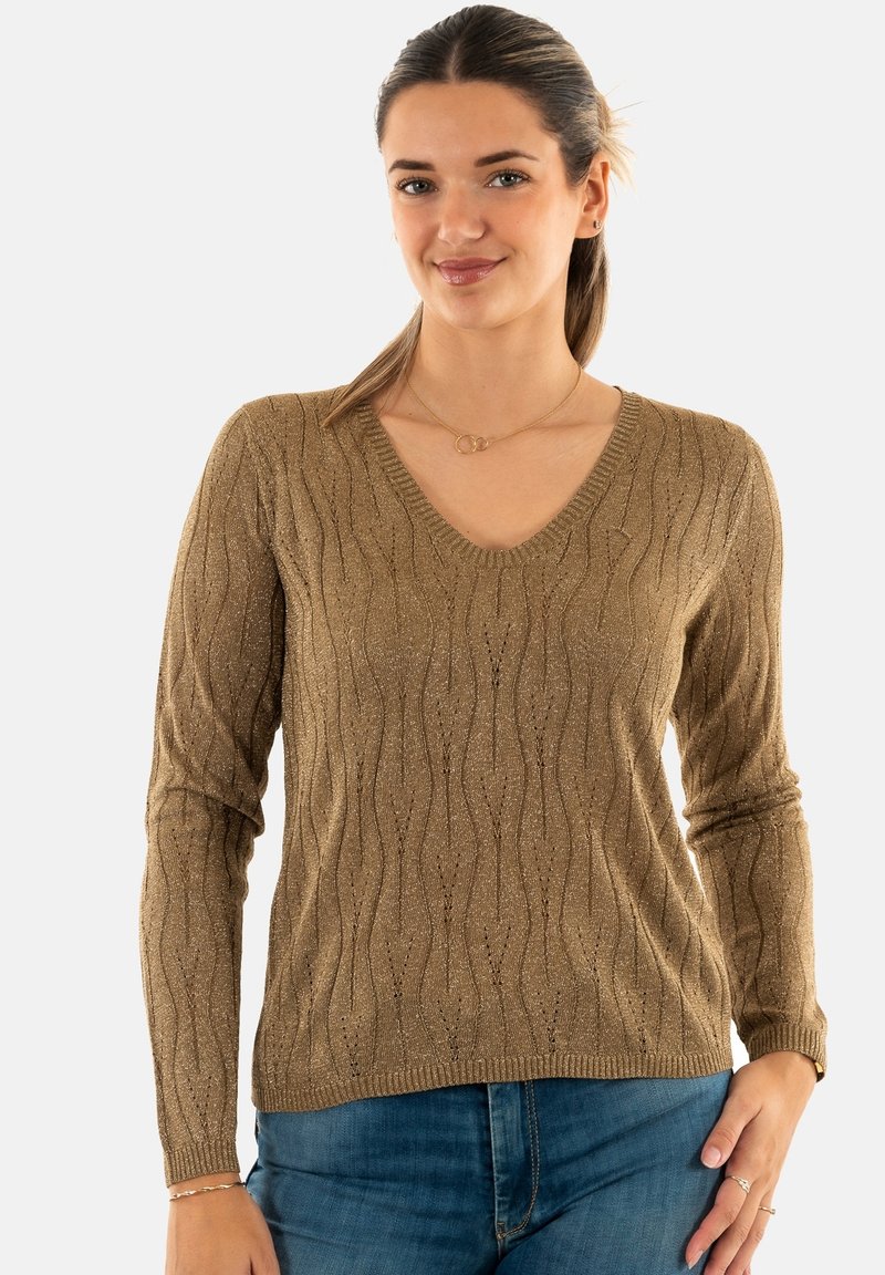Maglione a maniche lunghe con scollo a V in un tessuto metallico dorato texturizzato con un motivo a onde. Abbinato a jeans blu, collana sottile visibile.