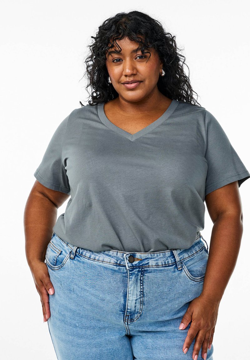 T-shirt grigio a scollo a V con maniche corte, realizzato in tessuto morbido. Abbinato a jeans in denim a vita alta di colore blu chiaro con chiusura a bottoni.