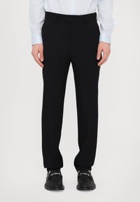 Zwarte op maat gemaakte broeken met een gladde textuur, rechte pasvorm en een platte voorkant. Draagt een lichtblauw overhemd met lange mouwen.