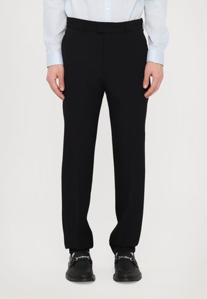 Pantalons noirs ajustés avec une texture lisse, une coupe droite et un design à plat. Portés avec une chemise à manches longues bleu clair.