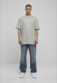Grå oversized t-skjorte med kortermet, kombinert med lyseblå, løstsittende jeans og hvite joggesko, mot en enkel grå bakgrunn.