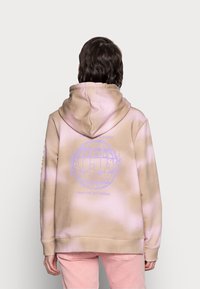 Béžová mikina s kapucí a růžovým tie-dye vzorem. Na zádech má fialový grafický design a vroubkované manžety a lem.