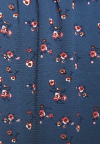 Blått tyg med små blommönster i rosa och brunt, med en texturerad yta och veck som skapar ett mjukt, strukturerat utseende.