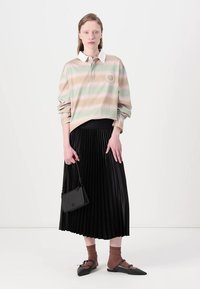 Camisa polo listrada em cores pastel com colarinho branco, combinada com uma saia preta pregueada. A modelo segura uma pequena bolsa preta e usa meias castanhas com sapatos pretos.