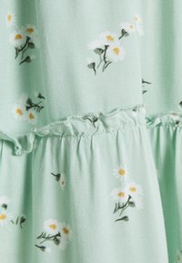 Blommig klänning i mjukt minttyg, med vita prästkragar med gula mittar. Volangkant och texturerad yta förbättrar designen.