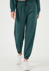 Pantaloni jogger turchesi realizzati in un tessuto morbido, con vita elasticizzata, cordino e polsini alle caviglie, abbinati a sneakers bianche.