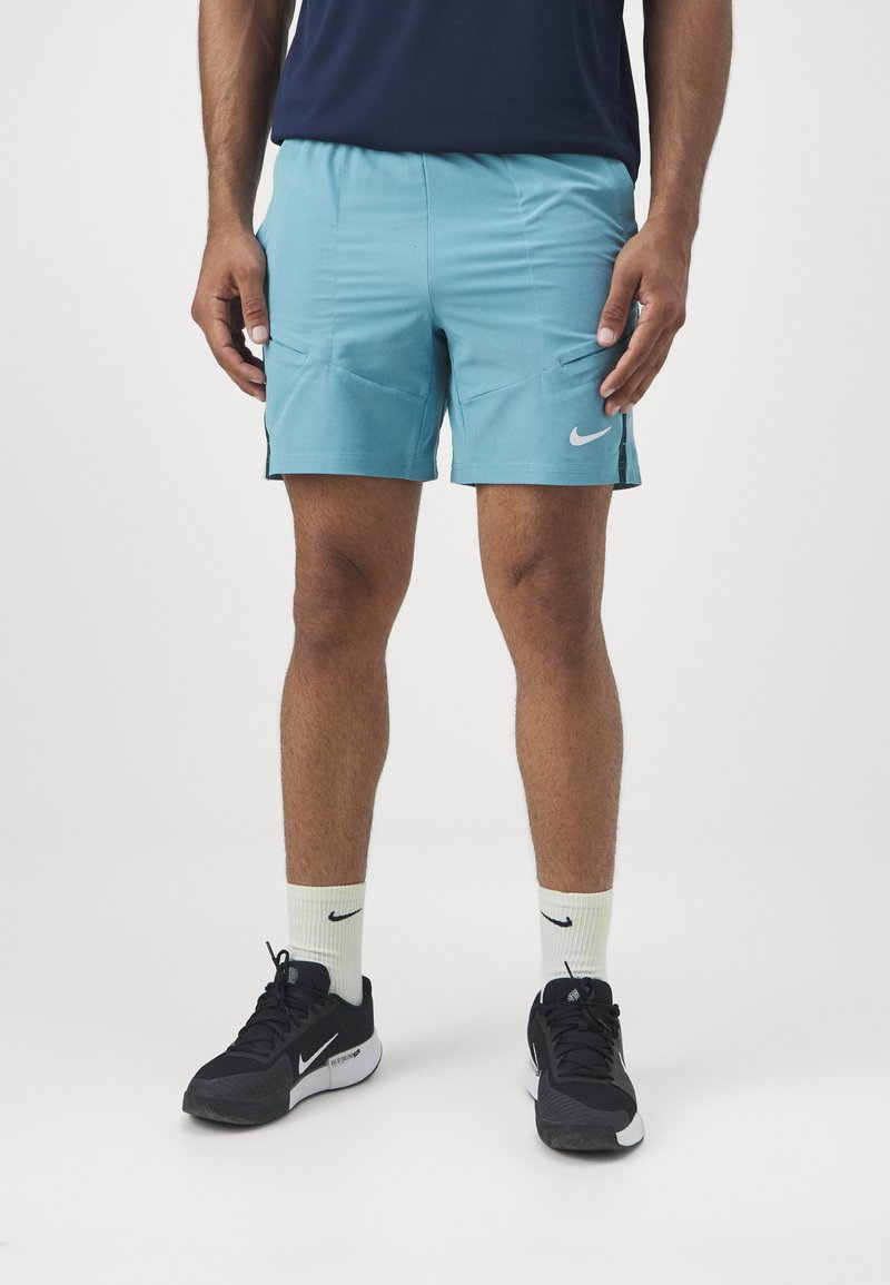 Pantalones cortos deportivos de color azul claro con bolsillos laterales, acentos negros y un logo de Nike blanco, combinados con zapatillas negras y calcetines de color claro.