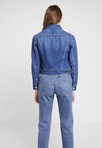 Denim jacket with a fitted design, medium blue color, and front buttons. Paired with high-waisted, light blue denim pants.