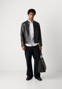 Schwarze Lederjacke mit Stehkragen, weißes Hemd mit Knöpfen, dunkle Jeans und eine schwarze Tragetasche. Glatte Textur und lässiges Design.