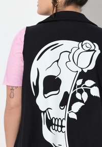 Schwarze Weste mit einem großen weißen Totenkopf-Graphic, das mit einer Rose und Blättern gestaltet ist, aus einem Stoff mit glatter Textur, über einem pinken Hemd getragen.