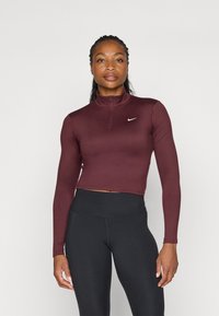 Bordeaux fôret zip-up treningsgenser med lange ermer og høy krage, med en liten hvit Nike-logo på venstre bryst. Sorte høytlivs leggings.