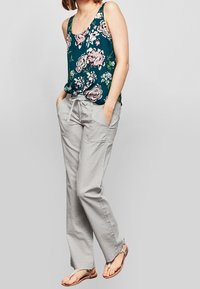 Débardeur floral en teal avec des fleurs roses et blanches ; associé à un pantalon ample gris clair ; le modèle porte des sandales plates.