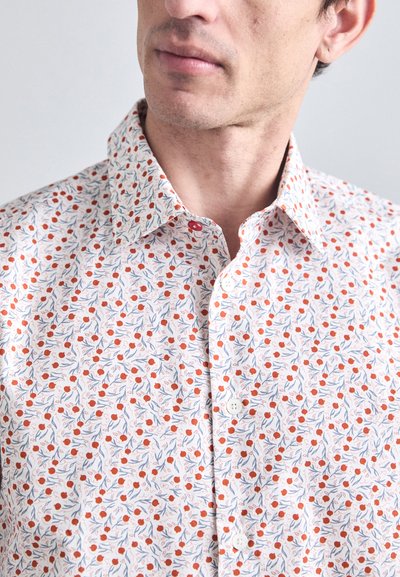 White shirt with an all-over floral pattern in red and blue, featuring a pointed collar and button placket, made from a lightweight fabric.