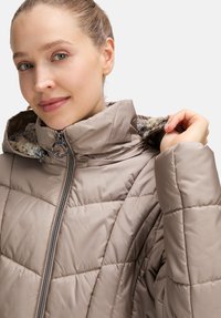 Beżowa pikowana kurtka z wysokim kołnierzem i zamkiem błyskawicznym. Posiada miękką, teksturowaną podszewkę oraz ukośny pikowany wzór.