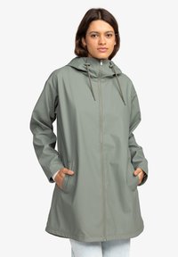 Capa de lluvia verde claro, impermeable, con capucha, cremallera frontal, cordón y bolsillos laterales, que presenta un ajuste relajado y una textura suave.
