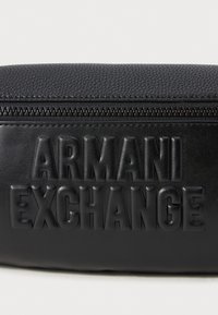 Schwarze, strukturiert Lederhandtasche mit einem auffälligen geprägten "ARMANI EXCHANGE"-Logo und einem glatten Reißverschlussverschluss an der Oberseite.